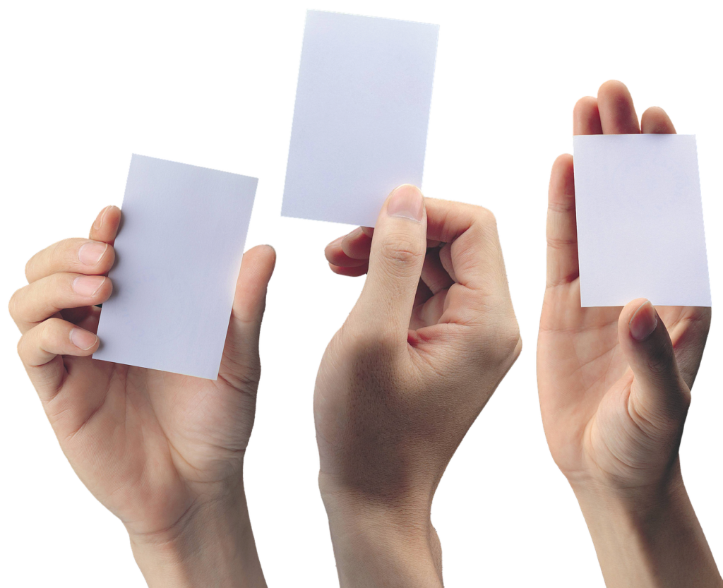 Three hands are shown holding up blank, white pieces of paper or cards. The hands are arranged such that they each hold one card, with the cards facing forward and no text or images visible on them. The background is plain, emphasizing the hands and cards—potentially symbolizing Medical Marijuana Cards yet to be issued.